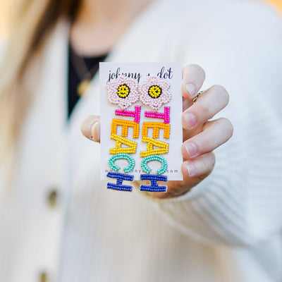 Model holding a pair of Beaded Floral TEACH Earrings for teachers. 